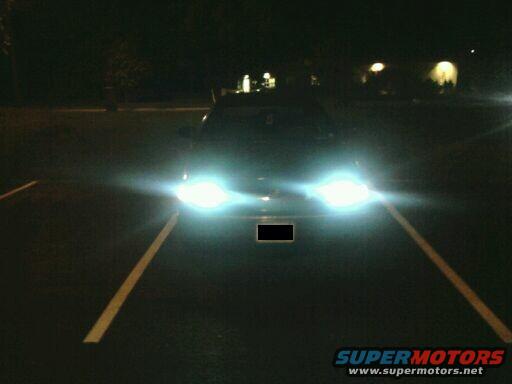 Car parked at night, headlights on bright. Parking lines visible