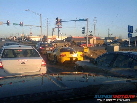 Yellow sports car with black racing stripes on the rear, stopped in traffic