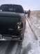 2005 Ford F-250 - A dark green Ford pickup truck is seen from the rear with a damaged taillight. A man walks away in the snowy background.