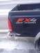 2005 Ford F-250 - Dark pickup truck with FX4 Off Road decal and damaged bumper, seen in winter conditions.