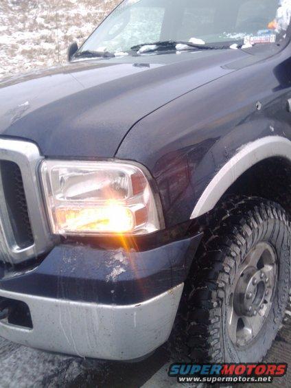 Dark blue 2005 Ford F-250 pickup truck front fender and headlight with turn signal illuminated
