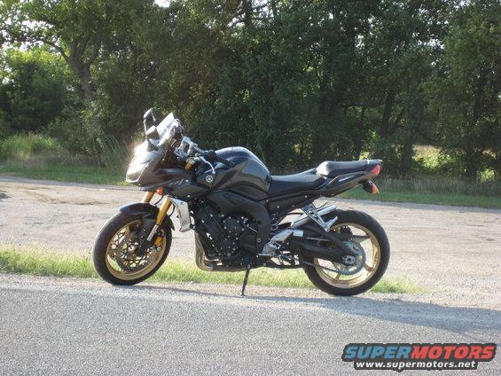 Dark motorcycle parked on the side of a road with trees in the background