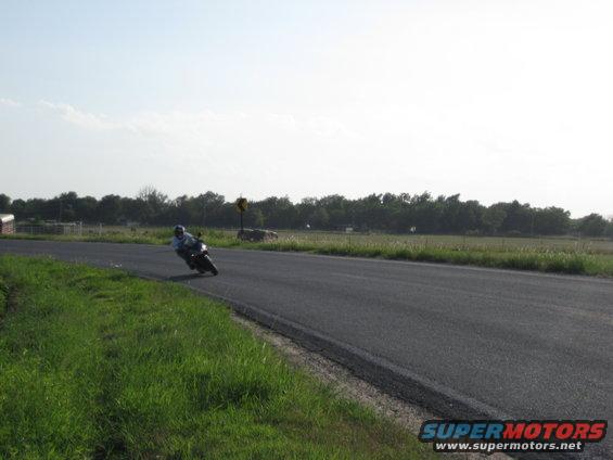 Motorcycle leaning into a turn on a rural road, rider wearing a helmet and light-colored shirt