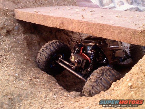 Black remote control rock crawler navigating a dirt path under a rock