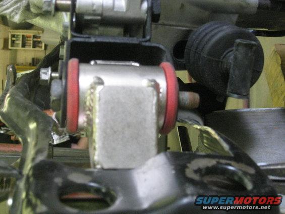 Close-up of a silver suspension component with red bushings, bolted to black metal