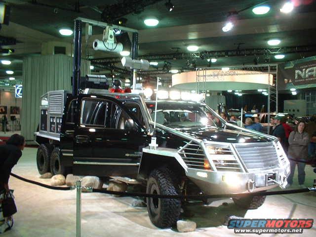 Black truck with a large grille and equipment mounted on top, seen at an auto show