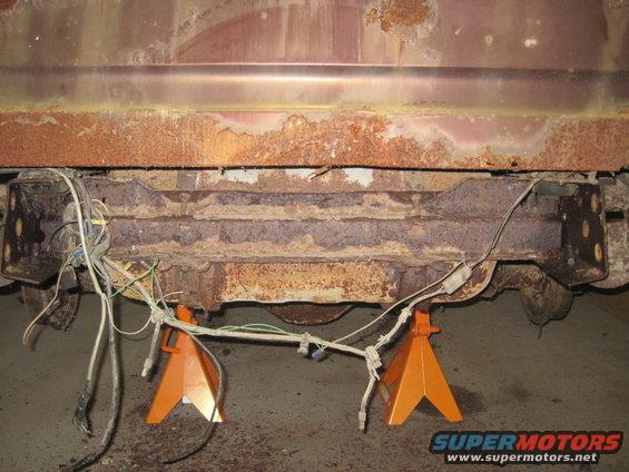 rusted rear frame and wiring on vehicle supported by jack stands