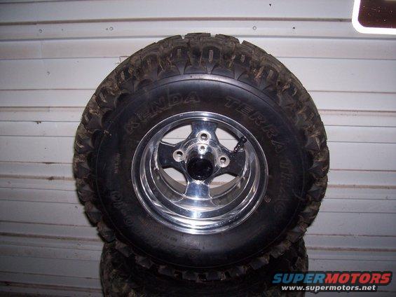 Tire with Kenda Terra Trac branding on a chrome five-spoke wheel, stacked on other tires