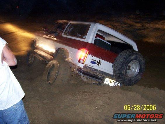 Ford Bronco stuck in mud at night, with headlights on