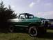 1979 Ford Bronco - Lifted green Ford Bronco with aftermarket wheels and tires sits on a grassy field under a partly cloudy sky.