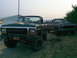 1979 Ford Bronco - Two Ford trucks, a green Bronco and a dark pickup, are parked outdoors under an overcast sky.