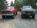 1979 Ford Bronco - Two lifted pickup trucks, a green 1979 Ford F-Series and a red Dodge, are parked on a gravel road.