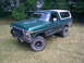 1979 Ford Bronco - Green Ford Bronco with white top, lifted with off-road tires and a "Let's Pit Stop" sticker.