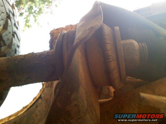 Close-up of a rusted suspension component, possibly a bushing or mount, with a tire visible on the left