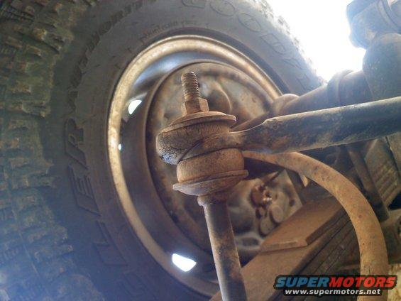 Close-up of a rusty ball joint and tie rod end with a tire and wheel in the background