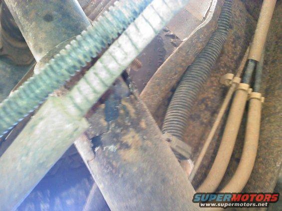 Undercarriage view of rusty metal parts and hoses, with a SuperMotors logo at the bottom right