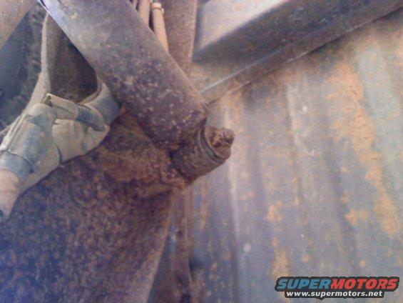 Rusty suspension part with a bolt head visible, attached to a metal bracket