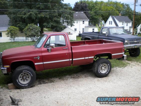 Red 1985 Chevrolet C/K Pickup parked next to a dark blue pickup truck