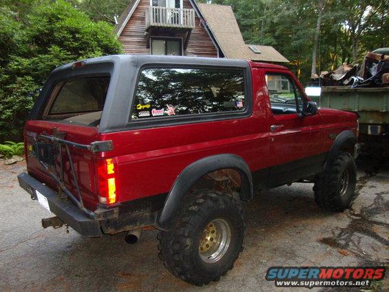 Red Ford Bronco with black trim, large off-road tires, and aftermarket rear bumper