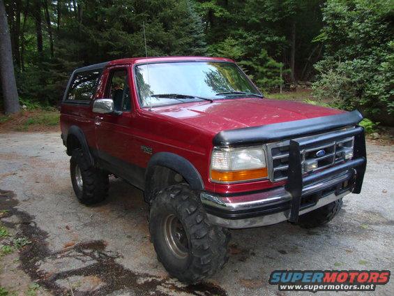 1995 Ford Bronco with large off-road tires and a brush guard parked on a dirt driveway