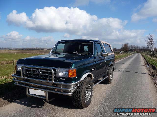 Dark green Ford Bronco with tan top and chrome bull bar parked on a rural road