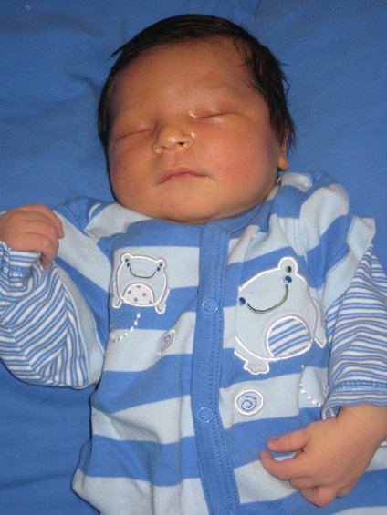 Newborn baby sleeping on blue fabric, wearing blue and white striped pajamas with frog graphics
