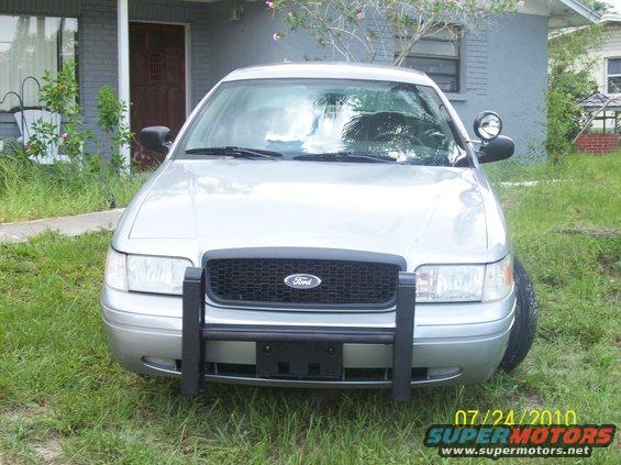 Front view of a silver 2003 Ford Crown Victoria police car with a push bar parked in front of a house