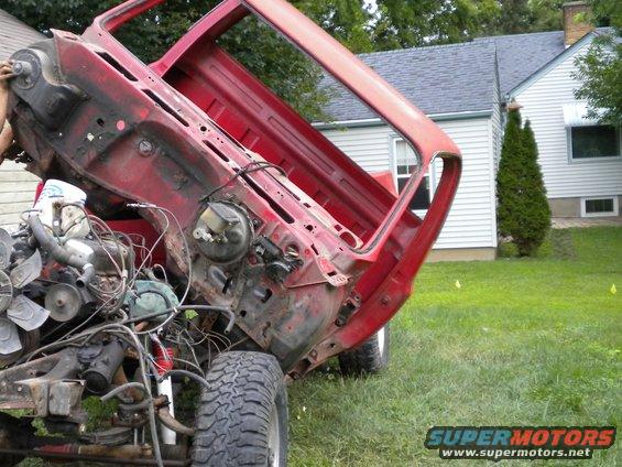 Red pickup truck chassis with engine exposed, tilted upwards, on grassy lawn