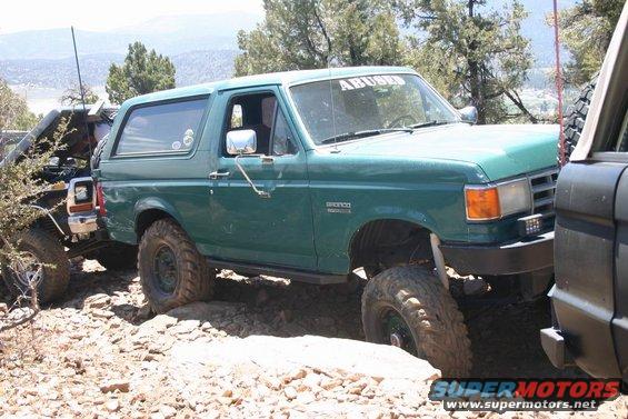 Green Ford Bronco with "ABUSED" sticker on windshield, off-roading on rocky terrain