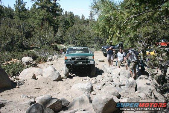 Green 1991 Ford Bronco navigating a rocky off-road trail with other vehicles and people present
