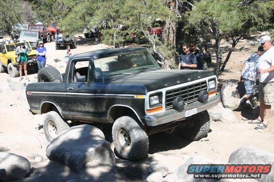 Black Ford Bronco off-roading over rocks, with a spare tire mounted in the bed