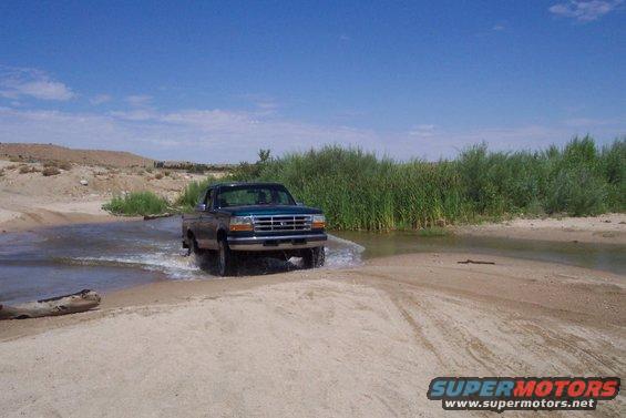 Green 1995 Ford F-150 driving through shallow water