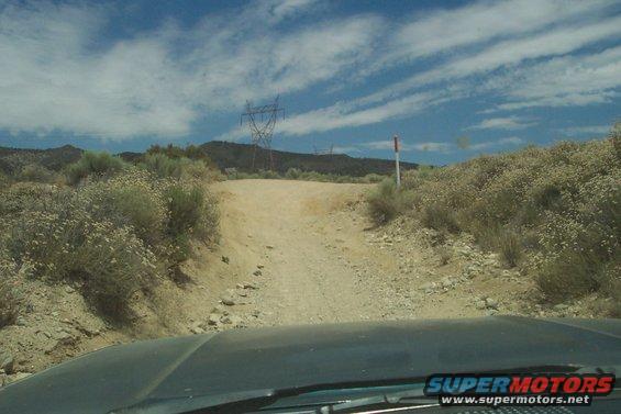 Dashboard view from a vehicle driving on a dirt road with scrub brush and power lines