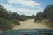 1995 Ford Bronco - Driving down a sandy, unpaved road surrounded by dense vegetation under a cloudy sky.