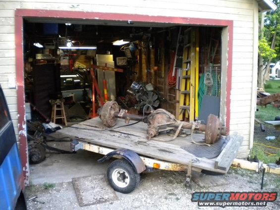 Two vehicle axles on a wooden trailer parked in front of an open garage