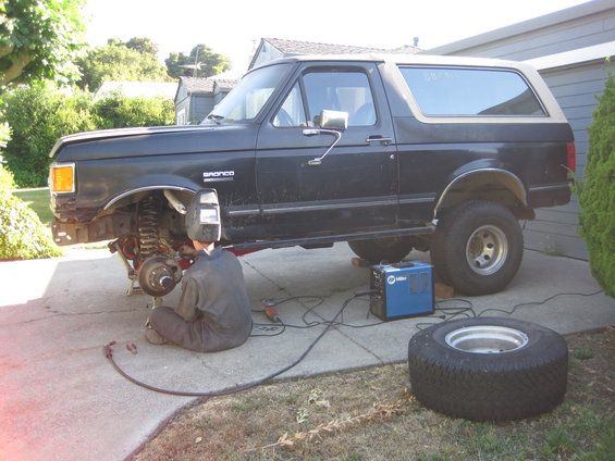 Guy in welding mask works on front suspension of a 1989 Ford Bronco. Miller welder nearby