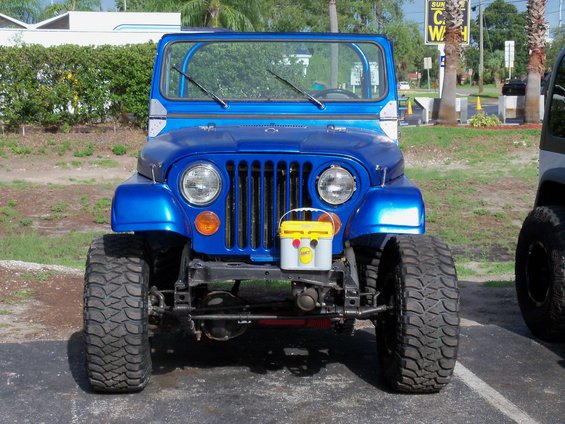 Front view of a blue 1978 Jeep CJ5 with large off-road tires and a yellow battery box mounted on the front