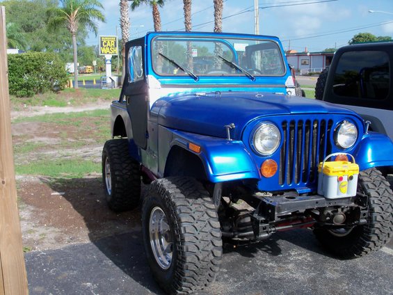 Blue Jeep CJ with aftermarket wheels and tires, parked outside