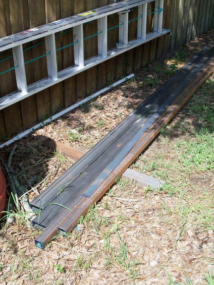 metal beams stacked on the ground next to a wooden fence with a ladder leaning against it