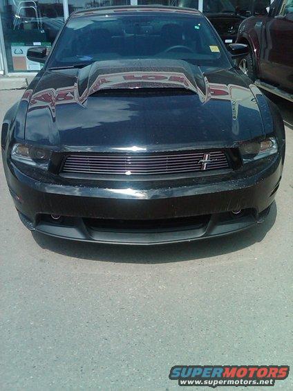 Black Ford Mustang with a prominent hood scoop and horizontal grille, viewed from the front