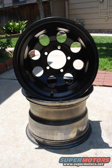 Two black rims stacked on a concrete surface. The top rim has circular cutouts