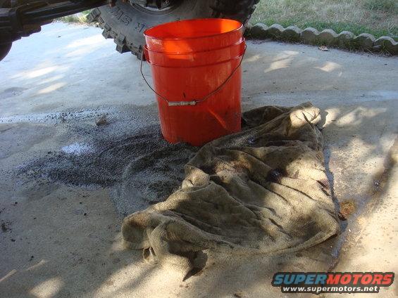Orange bucket and stained rag on concrete, with part of a tire and suspension visible