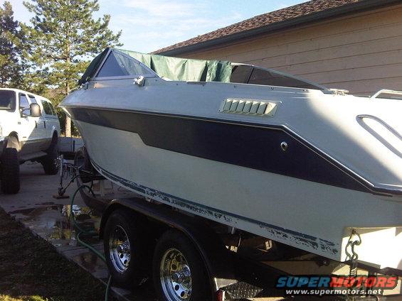 White boat with dark blue stripe on trailer, parked next to a white SUV