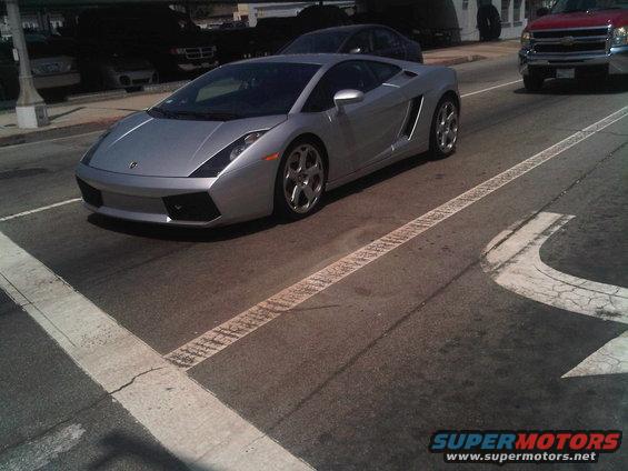 Silver Lamborghini Gallardo driving on a street, other cars in background