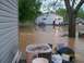 1974 Dodge 1500 - A green pickup truck sits in floodwaters in front of a house, with debris floating around.