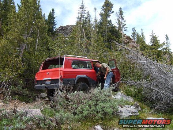 Red SUV with open doors parked on a rocky, wooded trail. Person is looking inside