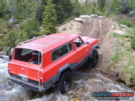 Red SUV driving through a stream on a dirt path in a forest