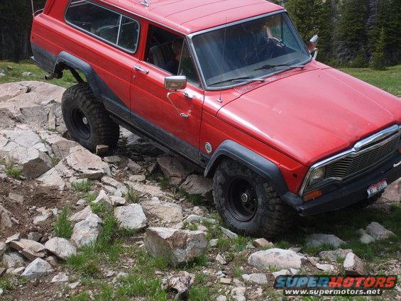 Red Jeep Cherokee Chief with large tires navigating rocky terrain