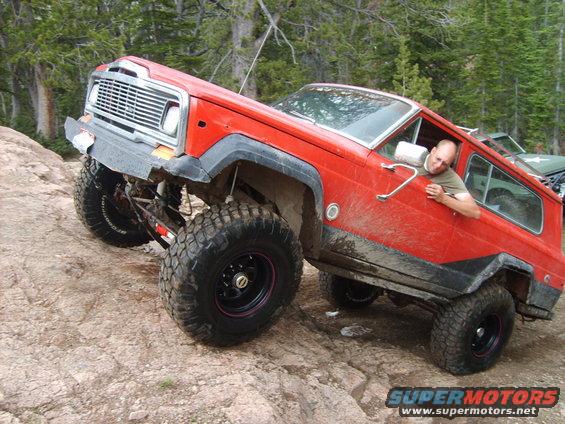 Red Jeep Cherokee climbing rocks, driver leaning out window. Another vehicle visible behind