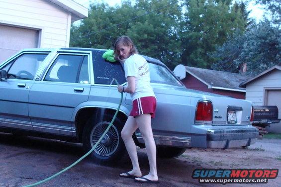 Woman washing the side of a light blue sedan. The car has chrome trim and wire wheel covers